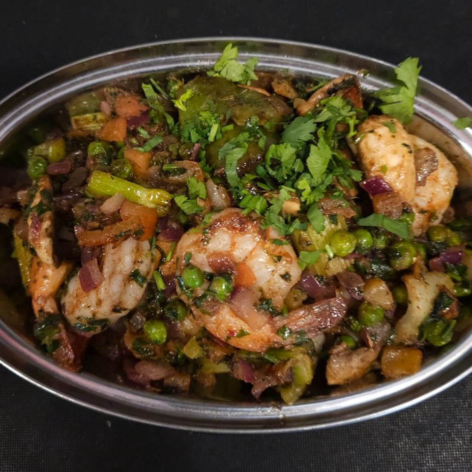 Close-up of Indian shrimp curry with peas, onions, and cilantro in a silver bowl.