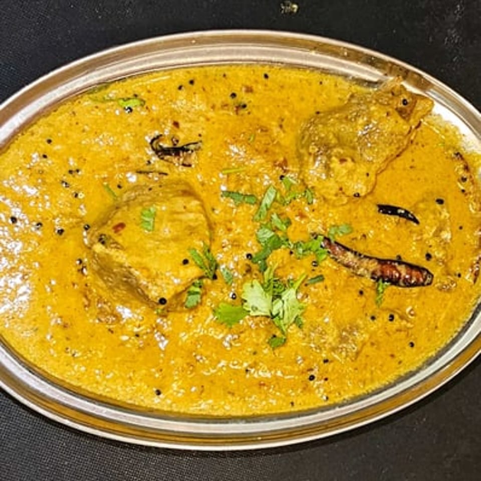 Indian chicken curry in a silver oval dish, garnished with cilantro and dried chilies.