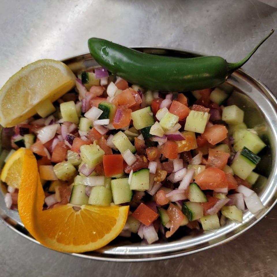 Diced Indian salad with tomatoes, cucumbers, and onions, garnished with lemon, orange, and a jalapeño.