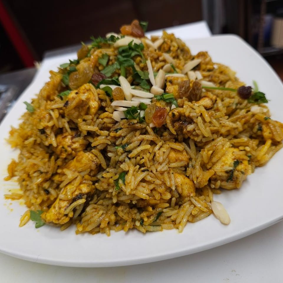 Chicken Biryani from Akbar Cuisine of India, garnished with cilantro, raisins, and slivered almonds.
