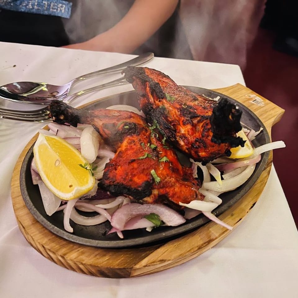 Two pieces of Tandoori Chicken on a sizzling platter with onions and lemon wedges.